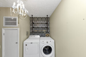 Laundry room with shelf, washer, dryer and a chandelier. The door to the furnace.