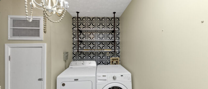 Laundry room with shelf, washer, dryer and a chandelier. The door to the furnace.