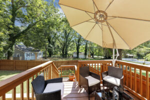 Back deck with umbrella open on a sunny day with patio furniture in a fenced in yard